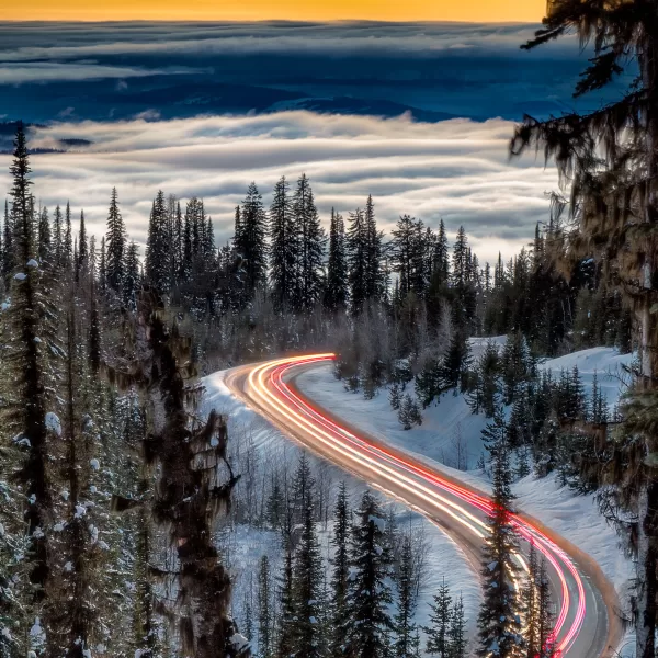 Light trails illuminate the road to Silver Star Mountain as cars climb the hill and rise above a thick sea of clouds that blanket the city below.